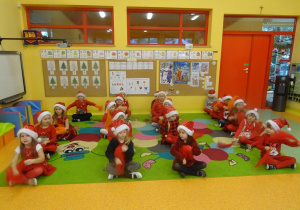Dzieci siedzą w czterech rzędach, trzymają w ręku czerwone chusteczki.